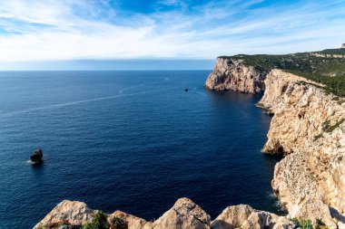 Derin mavi denize bakan kayalık kayalıklardan hafif bulutlu ve parlak mavi gökyüzünün altında sarp kıyı oluşumlarına bakın..
