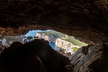 Kıyı mağarasının içinden, mağaranın açıklığından görünen kayalık tavanı ve duvarları, uzak uçurumları ve denizi gösteren bir görüntü..