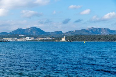 Denizden Olbia yakınlarındaki küçük bir yarımadadaki deniz fenerine doğru bir görüntü. Arkasında dağlar ve sanayi binaları var..