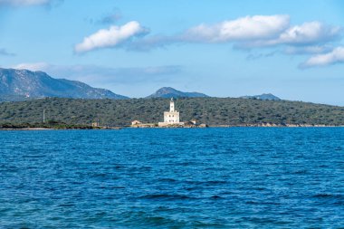 Derin mavi deniz ve Olbia yakınlarındaki tepelik yeşil manzarayla çevrili bir iskelede beyaz bir deniz feneri dağınık bulutlu bir gökyüzünün altında..