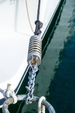 Metal bir demirleme yay ve zinciri, durgun yeşil sularda bir tekneyi emniyete alırken yüzeyde yansımalar görülebilir..