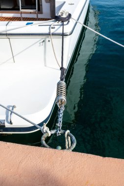 Bir yat, birçok halat, metal zincir ve derin yeşil su üzerinde paslanmaz çelik bir yay kullanılarak bir iskeleye sabitlenir..