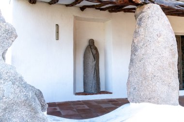 Sardunya, Porto Cervo 'daki Stella Maris Kilisesi girişinde granit sütunlar ve ahşap kirişlerle çerçevelenmiş beyaz bir duvar oyuğunda taş heykel..