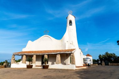 Porto Cervo 'daki Stella Maris Kilisesi' nin önü. Duvarları beyazlatılmış, taş sütunlar ve açık mavi gökyüzünün altında küçük bir çan kulesi var..