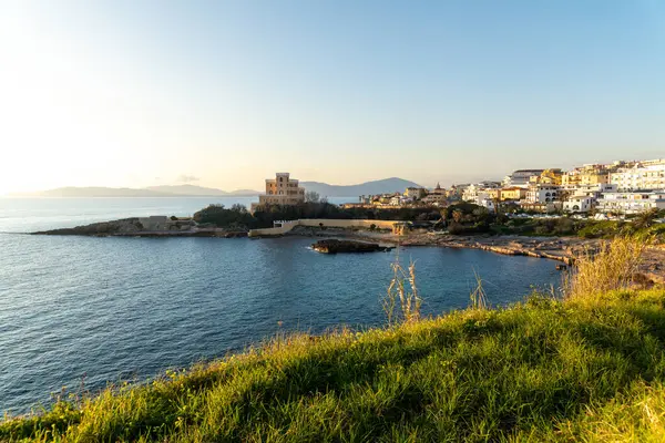 Tepede tarihi bir villası olan bir sahil koyunda. Sahil boyunca beyaz ve sarı evler. Çayır, tepeler ve sıcak akşam ışığında mavi gökyüzü..