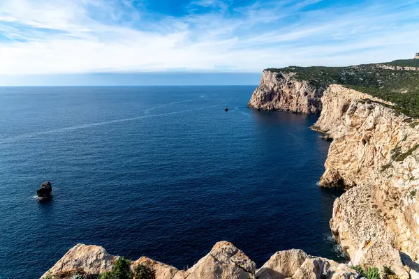 Derin mavi denize bakan kayalık kayalıklardan hafif bulutlu ve parlak mavi gökyüzünün altında sarp kıyı oluşumlarına bakın..