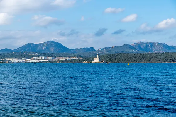 Denizden Olbia yakınlarındaki küçük bir yarımadadaki deniz fenerine doğru bir görüntü. Arkasında dağlar ve sanayi binaları var..