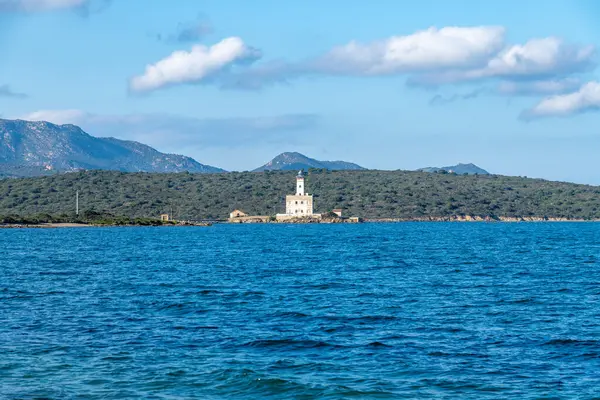 Derin mavi deniz ve Olbia yakınlarındaki tepelik yeşil manzarayla çevrili bir iskelede beyaz bir deniz feneri dağınık bulutlu bir gökyüzünün altında..