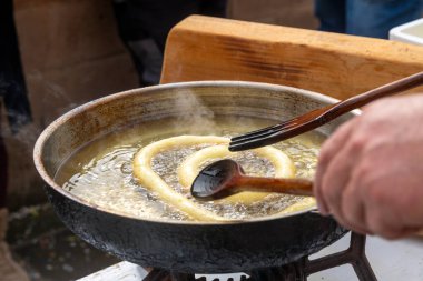 Bir hamur halkası, geleneksel bir yemek pişirme ya da sokak yemeği hazırlama sahnesinin bir parçası olan tavadaki ahşap kaplar kullanılarak kaynayan yağda kızartılıyor..