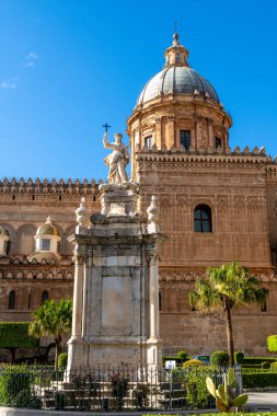 Palermo Katedralleri 'nin önünde haç tutan mermer heykel ayrıntılı cephe ve arka planda açık mavi gökyüzü ile duruyor..