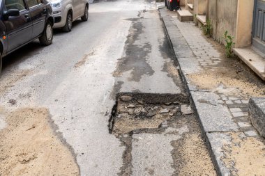 Sert, pürüzlü bir yüzeyi ve bir sokak boyunca görünen yeraltı taşları olan asfalt parçası bir binanın girişinin yanında..