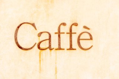 Paslı metal harfler, Scicli 'de dokulu bej bir duvara monte edilmiş Caffe kelimesini oluşturuyor..