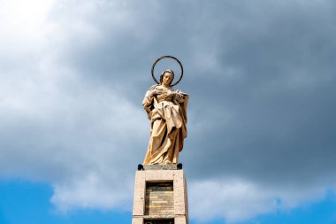Mavi yamalı bulutlu bir gökyüzüne karşı duran ve yukarıdan yayılmış gün ışığına sahip bir azizin heykeli..