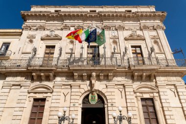 Sicilya, Syrakus 'taki Palazzo Civico cephesinde süslü taş detaylar, dekoratif balkonlar, bölgesel, İtalyan ve Avrupa bayrakları.
