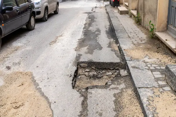 Sert, pürüzlü bir yüzeyi ve bir sokak boyunca görünen yeraltı taşları olan asfalt parçası bir binanın girişinin yanında..