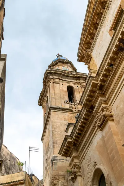 Sicilya Ragusa 'da bulunan bulutlu bir gökyüzünün altında eski taş binalarla çevrili tarihi bir kilise çan kulesi manzarası..