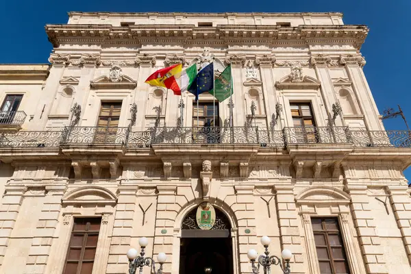 Sicilya, Syrakus 'taki Palazzo Civico cephesinde süslü taş detaylar, dekoratif balkonlar, bölgesel, İtalyan ve Avrupa bayrakları.