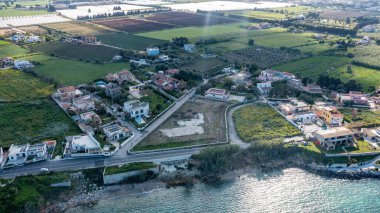 Syrakus, Sizilien - İtalya - 04-10-2025: Çevresi tarım arazileri, seralar ve kesişen yollar ve çeşitli bitkilerle çevrili tarlalarla çevrili kıyı muhitinin havadan görünüşü