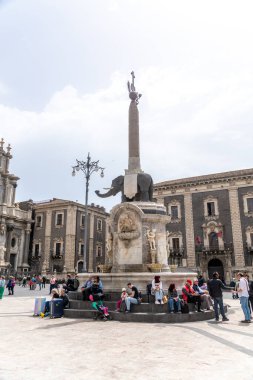 Catania, Sizilien - İtalya - 04-15-2025: İnsanlar arka planda barok binalar, heykeller ve dikilitaşlarla Catania 'nın Piazza del Duomo kentindeki Fil Çeşmesi etrafında oturdular.