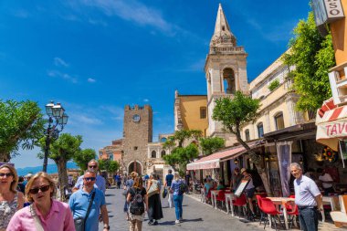 Taormina, Sizilien - İtalya - 05-04-2025: Taormina, Sicilya 'daki Piazza IX Aprile, Chiesa di San Giuseppe, saat kulesi, çizgili restoran tenteleri, turistler ve açık yaz gökyüzü.