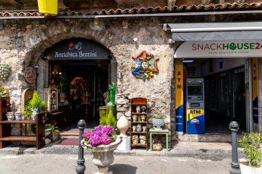 Taormina, Sizilien - İtalya - 05-04-2025: Taormina, Sicilya 'da sokak manzarası Antichita Bettini antika dükkanı, renkli seramik, bitkiler ve ATM' yi bir büfe girişinin yanında gösteriyor.
