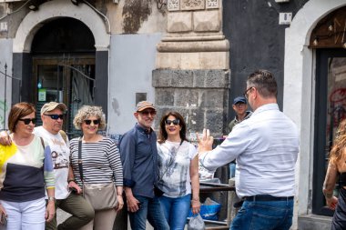 Catania, Sizilien - İtalya - 04-15-2025: Altı turist sokakta grup fotoğrafı için poz verirken, bir diğeri önde durup akıllı telefonuyla fotoğraflarını çekiyor.