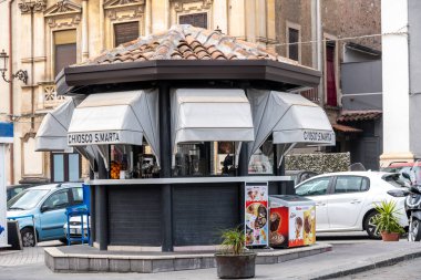 Catania, Sizilien - İtalya - 04-15-2025: Catania 'da fayans çatılı sokak büfesi, içecek makineleri, tenteler, dondurma reklamları ve arka planda park halindeki arabalar