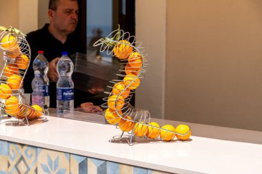 Taormina, Sizilien - İtalya - 05-04-2025: Portakallarla birlikte Sicilya 'nın Taormina kentindeki bir tezgahta bir adam ve arka planda bir şişe suyla birlikte metal spiral bir tutacakta sergilenecek.