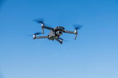 Syrakus, Sizilien - İtalya - 04-10-2025: Kameralı ve dönen pervaneli Quadcopter İHA, gündüz operasyonu sırasında açık mavi gökyüzüne karşı yakalandı.