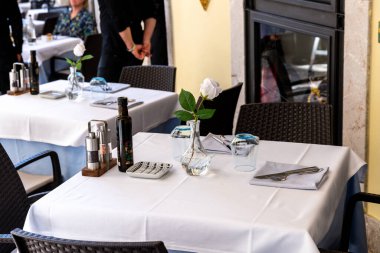 Taormina, Sizilien - İtalya - 05-04-2025: Taormina, Sicilya 'daki restoran masası, beyaz masa örtüsü, vazoda beyaz gül, zeytinyağı şişesi, cam eşyalar ve güzelce düzenlenmiş çatal bıçak takımı.