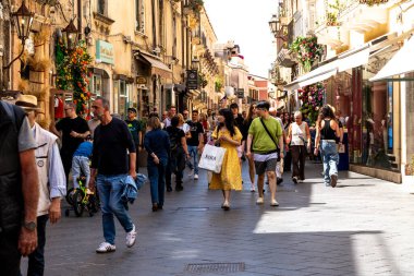 Taormina, Sizilien - İtalya - 05-04-2025: Sicilya 'nın Taormina kentinde tarihi binalar ve vitrinlerle çevrili canlı bir alışveriş caddesinde kalabalıklar yürüyor.