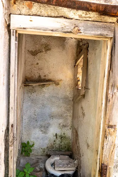 Graniti, Sizilien - İtalya - 05-05-2025: Kırık koltuklu terk edilmiş tuvalet, küflü duvarlar ve ahşap kapı çerçevesi, Graniti, Sicilya 'da ufalanan bir alanda ışığa maruz kaldı.