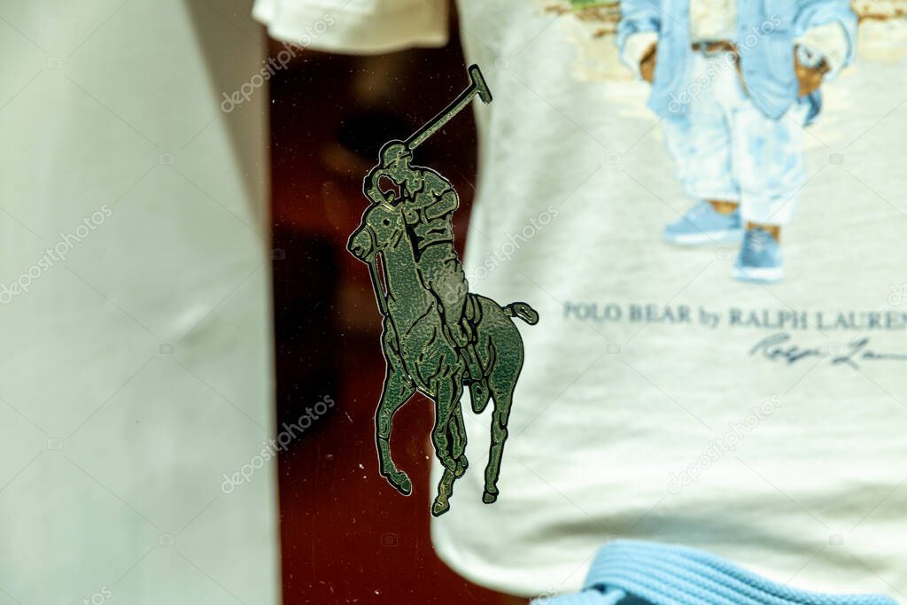 Taormina, Sizilien - Italy - 05-04-2025: Polo player silhouette on glass in front of Ralph Lauren bear T-shirt display in Taormina, Sicily, with visible blue clothing detail.