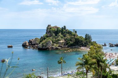 Taormina, Sizilien - İtalya - 05-04-2025: Bereketli bitki örtüsü, kayalık kıyıları ve yüzen ve güneşlenen turistlerle Isola Bella 'nın havadan görünüşü. Konum: Taormina, Sicilya.