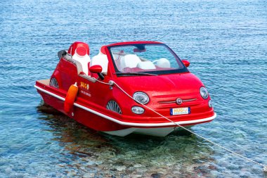 Taormina, Sizilien - İtalya - 05-04-2025: Kırmızı pedallı tekne beyaz koltuklu ve plakalı bir Fiat 500 gibi, Sicilya, Taormina yakınlarında sığ, açık mavi denizde yüzüyor..