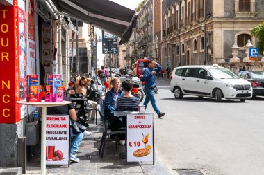 Catania, Sizilien - İtalya - 04-15-2025: Catania, Sicilya 'da sokak manzarası açık kafe, oturma konukları, reklam tabelaları, taksi ve yayalar tarihi kent binaları boyunca.
