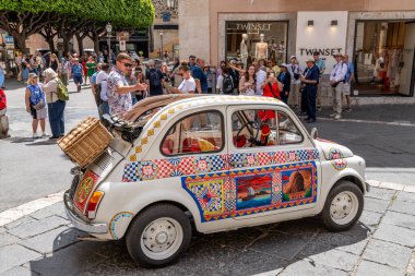 Taormina, Sizilien - İtalya - 05-04-2025: Meşgul bir caddeye park edilmiş renkli Sicilya motifleri ve hasır sepetli Fiat 500. Konum: Taormina, Sicilya, şehir merkezi.
