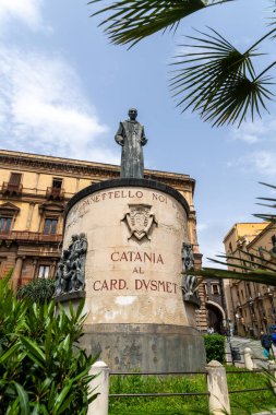 Catania, Sizilien - İtalya - 04-15-2025: Sicilya 'nın Katanya kentindeki silindirik bir üste Kardinal Giuseppe Dusmet' in heykeli, yardım figürleri, palmiye yaprakları ve binalarla çevrili.