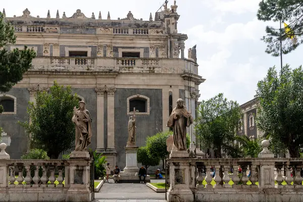 Catania, Sizilien - İtalya - 04-15-2025: Catania 'daki SantAgata Manastırı' nın önünde barok heykeller, balüstralar ve ön planda oturan ziyaretçiler.