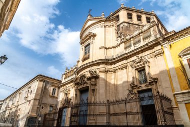 Catania, Sizilien - İtalya - 04-15-2025: Catania 'daki Chiesa di San Giuliano cephesi barok kıvrımlı, süslü taş işçiliği, kemerli kapılar, arka planda demir çit ve temiz gökyüzü.
