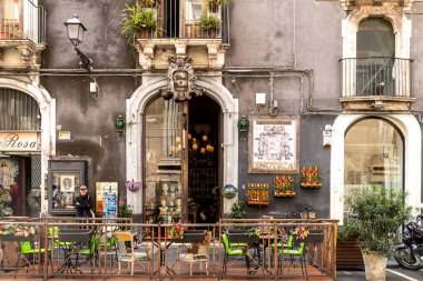 Catania, Sizilien - İtalya - 04-15-2025: Katanya, Sicilya 'da kemerli girişi, Enoteca tabelası, açık hava koltuğu, saksı bitkileri ve yakınlarda duran bir kişi.