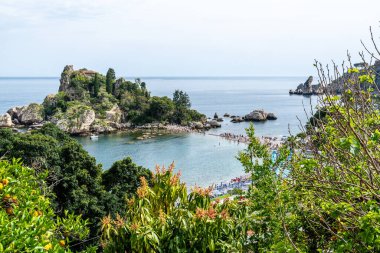 Taormina, Sizilien - İtalya - 05-04-2025: Yukarıdan görülen Isola Bella manzarası yemyeşil bir ada, berrak deniz, kayalık kıyı şeridi ve Sicilya 'nın Taormina kentindeki kalabalık plajı gösteriyor..