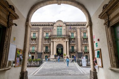 Catania, Sizilien - İtalya - 04-15-2025: Katanya 'daki San Nicola Manastırı' nın girişi kemer yoluyla, barok cephe, yeşil pencereler, balkonlar ve ön plandaki insanlarla görüldü.