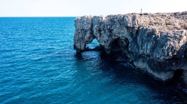 Sakin mavi okyanus suyuyla kaplı büyük kayalık bir kemer görünür erozyon desenleri ve parlak gökyüzünün altında gün ışığında dalgalı kıyı şeridi.