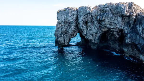 Sakin mavi deniz ve açık bir günde parlak gökyüzü ile çevrili engebeli sahil uçurumundan yükselen muazzam doğal kaya kemeri oluşumu..