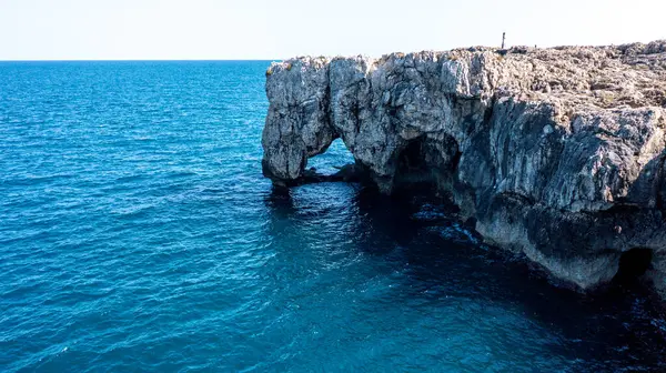 Sakin mavi okyanus suyuyla kaplı büyük kayalık bir kemer görünür erozyon desenleri ve parlak gökyüzünün altında gün ışığında dalgalı kıyı şeridi.
