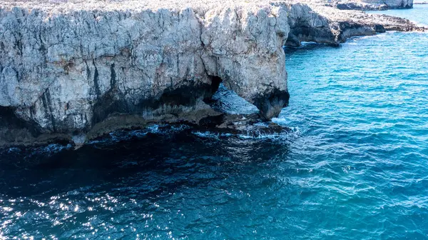 Doğal deniz mağarası engebeli sahil kayalıklarında turkuaz su ve görünür kaya dokularıyla kıyı şeridi yakınlarında gün ışığı altında..