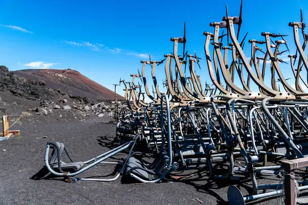 Etna Dağı yakınlarındaki karanlık volkanik zeminde metal çerçeveli kullanılmamış kayak kaldırma koltukları. Arka planda krater görülebilir..