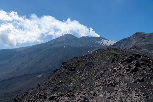 Volkanik arazi, Etnas Dağı zirvesi manzaralı kayalık yamaçlar, seyrek bitki örtüsü ve açık mavi gökyüzü ile beyaz duman yayıyor..