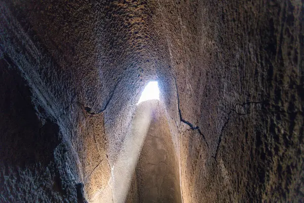 Güneş ışığı, Etna Dağı 'ndaki yüksek lav tüpündeki üçgen bir delikten içeri girer ve engebeli volkanik mağara duvarlarına bir ışık demeti oluşturur..
